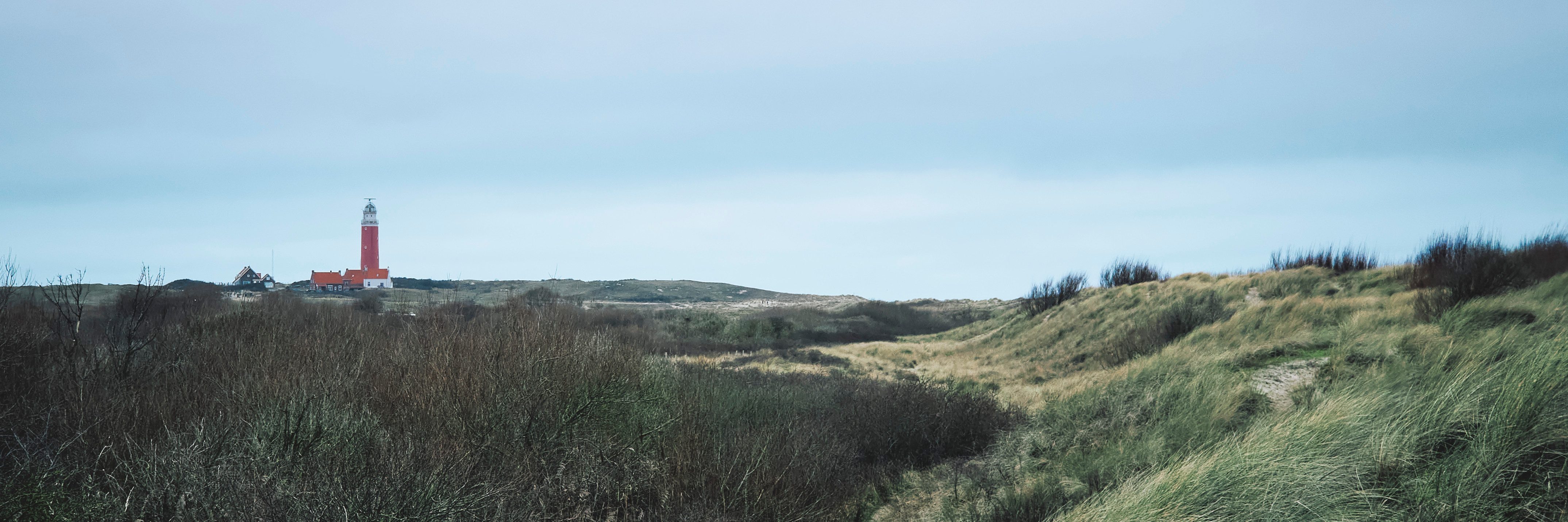 Red lighthouse standing alone in Dutch dunes against overcast atmospheric sky